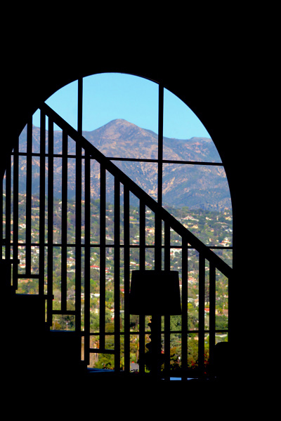 a Silhouette Image of a Larch Round Top Picture Window and Modern Spanish Stair Railing with a View of Santa Barbara, California in the Backdrop