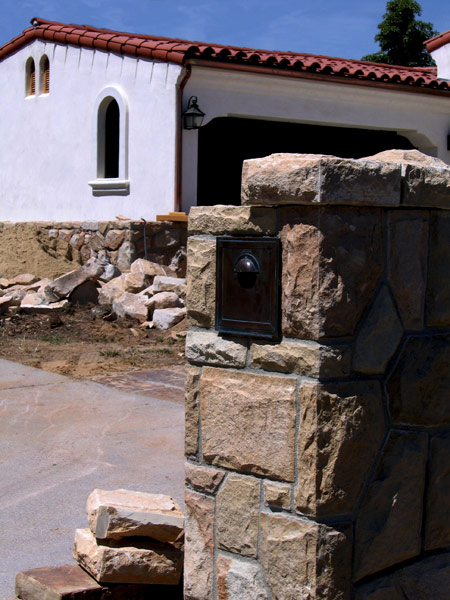 A construction photo showing local Santa Barbara California sandstone being incorporated into a custom stone mailbox, as well as sandstone garden walls up near the garage wall.