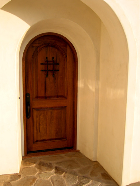 A custom Spanish style entry tower wood door is deeply recessed into the exterior stucco and features a flagstone entry landing in front of it.