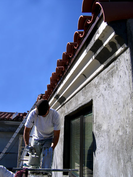 A young man in the stucco trade installing exterior architectural foam detail on a custom Spanish style small home renovation in Santa Barbara, California