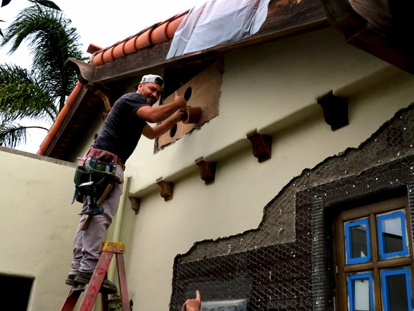 A young carpenter gives a thumbs up while installing Spanish clay vent pipes in the eave of a Spanish-style home in Santa Barbara, CA.