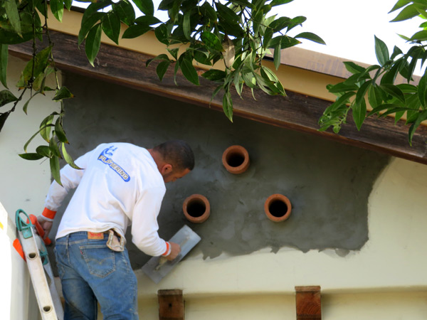 A professional plasterer applying stucco around clay vent pipes that are ventilating an attic space of a Spanish-style home in Santa Barbara, CA.