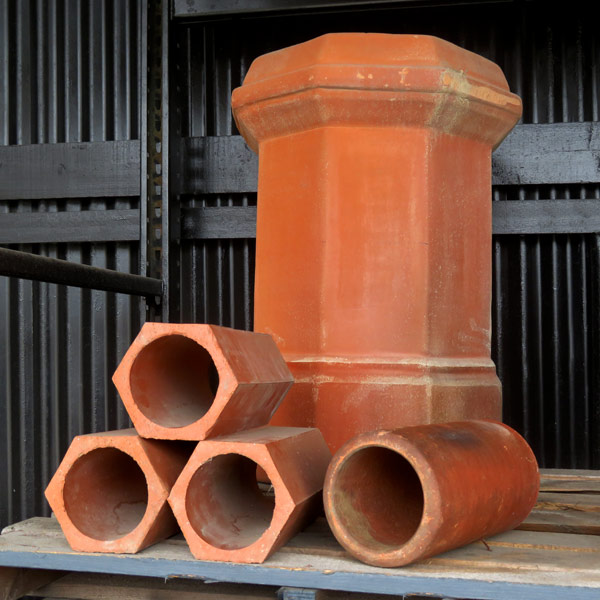A photo of terracotta clay drain pipes in hexagon shape and round shape, with a terracotta clay chimney pot in the background. Photo taken at Santa Barbara Stone in Santa Barbara, CA.