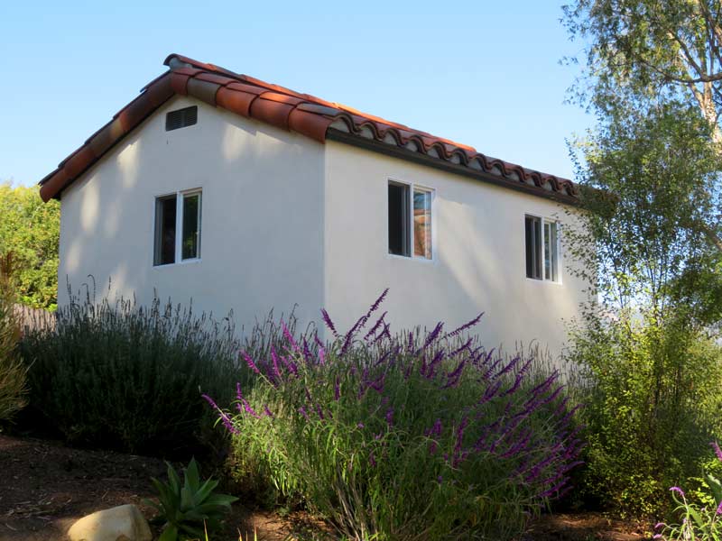Spanish style garden shed with red tile roof, white windows and smooth stucco