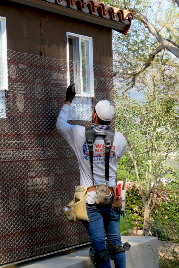 A stucco expert applies weatherproofing and wire to a spanish shed in the making.