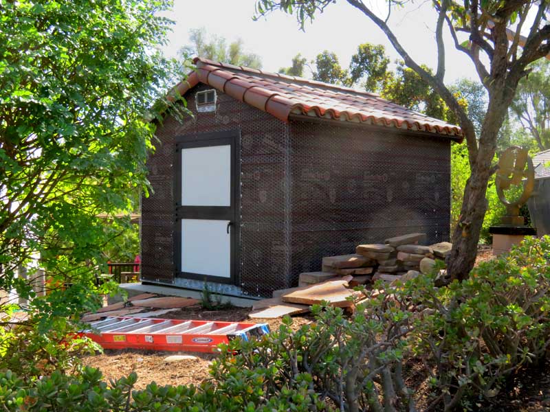 A standard shed is in the process of being transformed into spanish style with red tile roof and weatherproofing for stucco